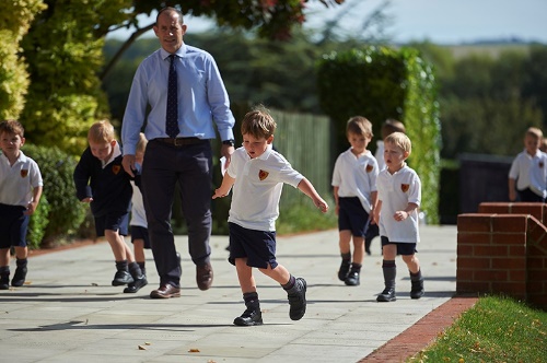A group of young students walking in school grounds with their teacher