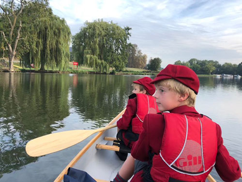 Two students in red uniforms are kayaking in a lake