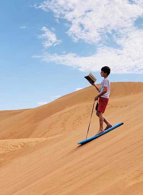 A student is reading a book on a sandy inclined slope
