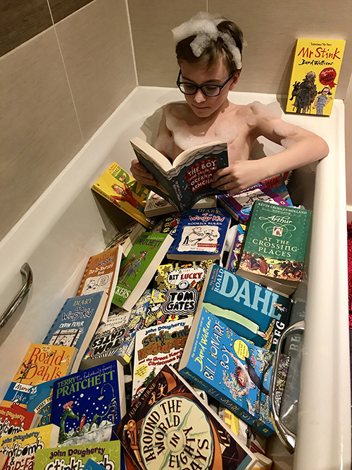 A student reading a book in a bath tub filled with books